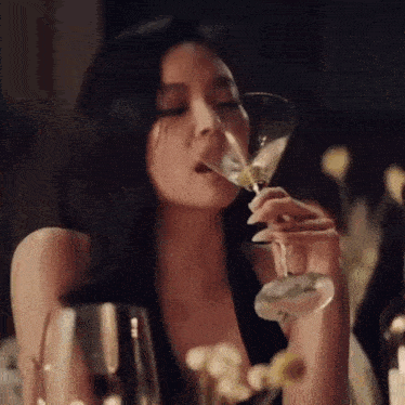 a woman is drinking a martini from a glass at a table .