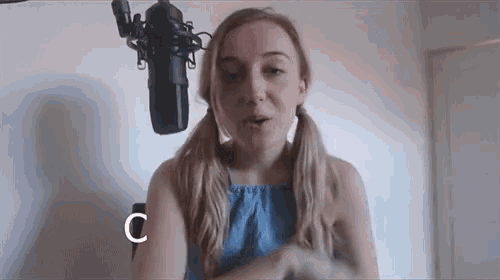 a woman with pigtails stands in front of a microphone with the letter c above her head