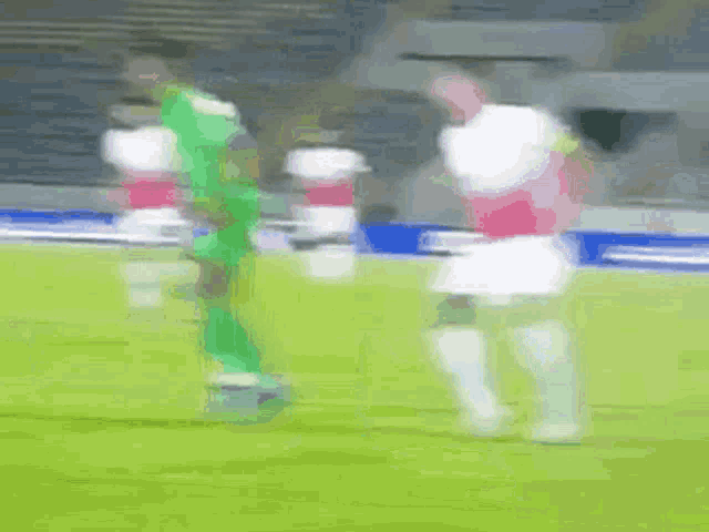 a blurry picture of soccer players on a field with a goalie in the background .