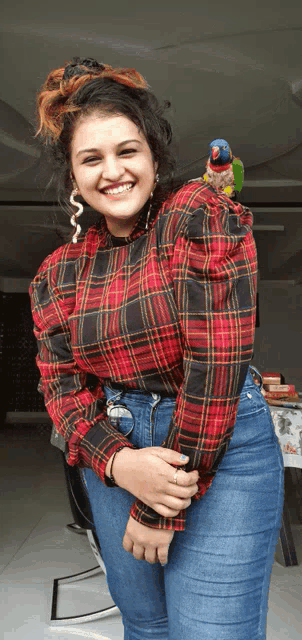 a woman in a plaid shirt smiles while holding a parrot on her shoulder