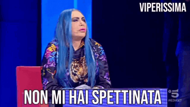 a woman with blue hair is sitting in front of a sign that says viperissima on it