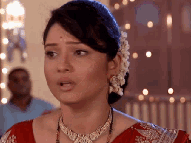 a woman wearing a red top and a necklace looks surprised