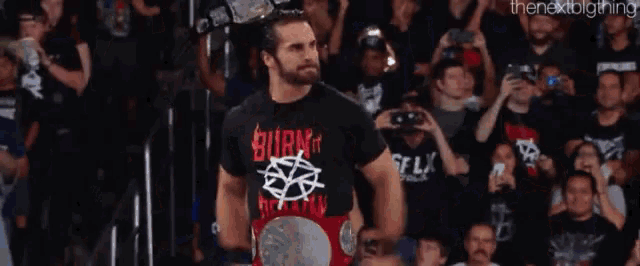a man in a burn it shirt is holding a championship belt in front of a crowd of people .