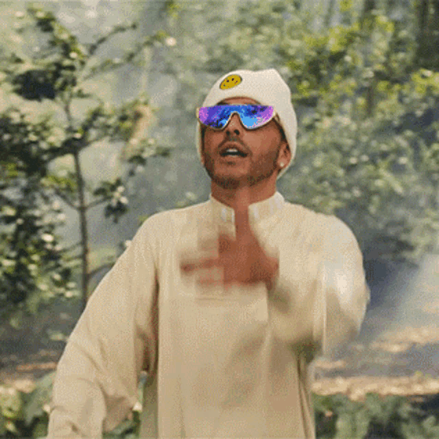 a man wearing sunglasses and a beanie has a yellow smiley face on his hat