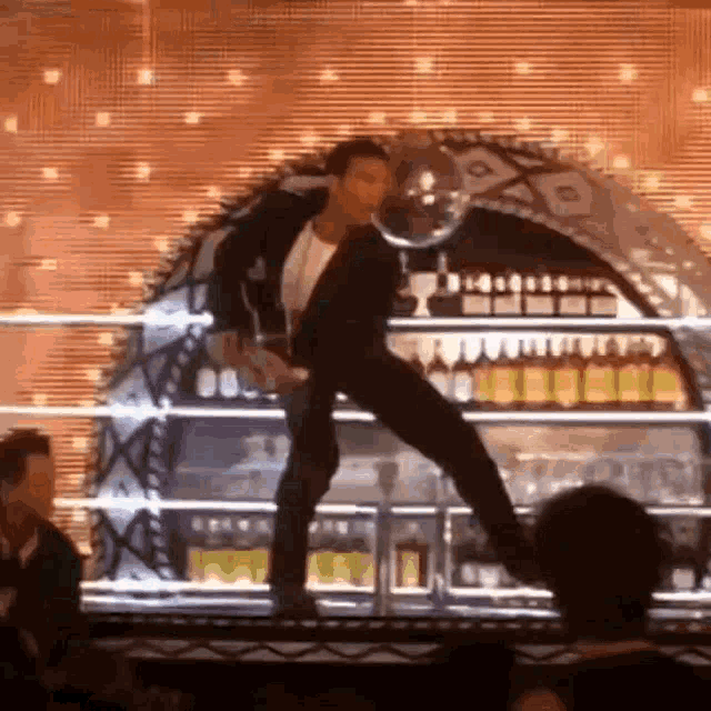 a man is dancing on a stage in front of a bar full of bottles of alcohol .