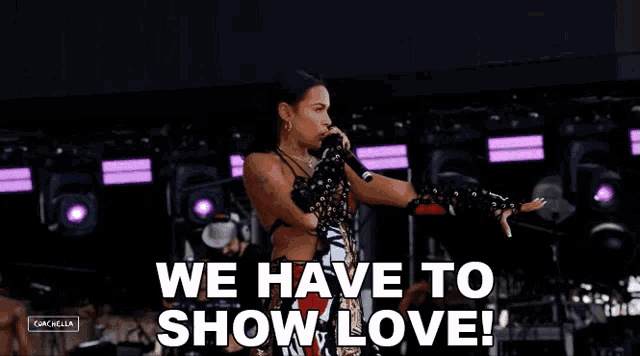 a woman singing into a microphone with the words we have to show love behind her .