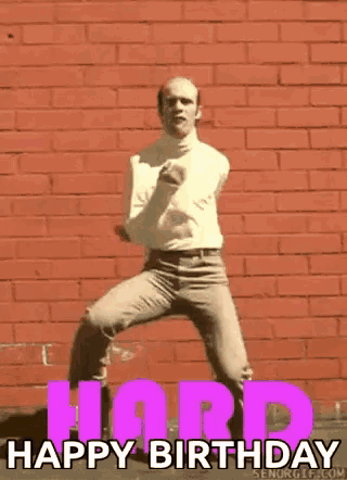 a man in a white turtleneck is dancing in front of a brick wall .