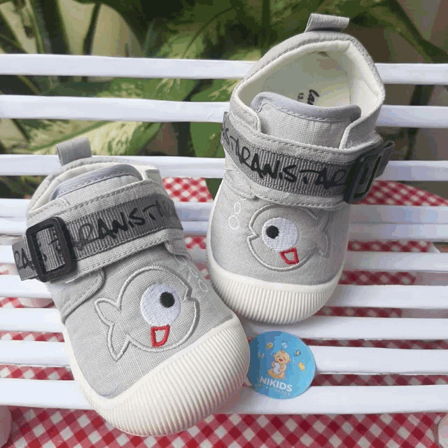 a pair of gray shoes with a fish embroidered on them are on a white bench
