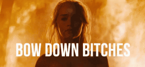 a woman is standing in front of a fire with the words `` bow down bitches '' written on the bottom .