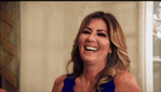 a woman in a blue dress is laughing and smiling in a room .