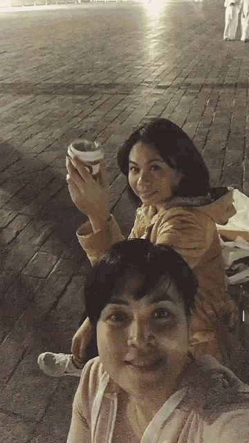 two women are posing for a picture while one is holding a cup