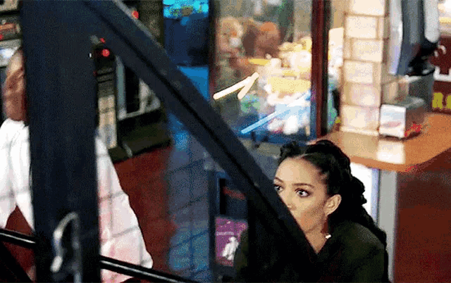 a woman looks out a window at a man playing a game in an arcade