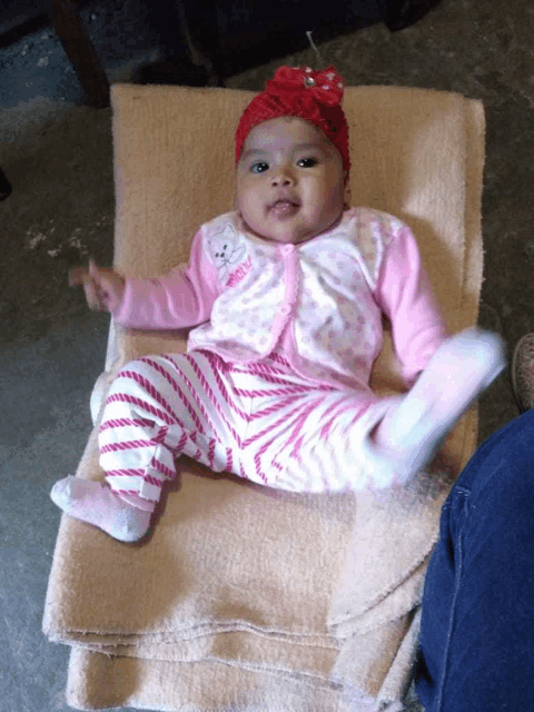 a baby wearing a pink cardigan and striped pants is laying on a blanket