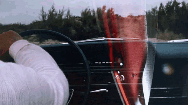a man is driving a car with a glass of wine in the back window
