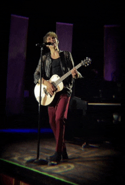 a man sings into a microphone while holding a guitar