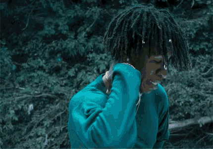 a man in a green shirt is tying his dreadlocks outdoors