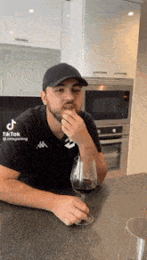 a man is sitting at a table with a glass of wine and eating a sandwich .