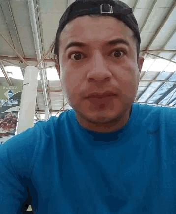 a man wearing a blue shirt and a baseball cap looks at the camera