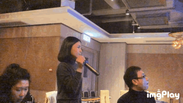 a woman singing into a microphone in a room with imgplay written on the bottom