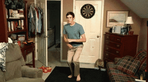 a man is dancing in a living room with a dart board on the wall