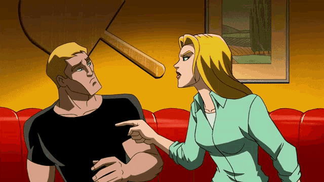 a man and a woman are sitting on a red couch and the woman is pointing at the man