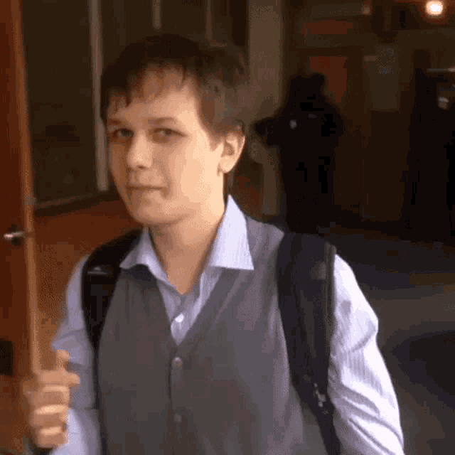 a young man wearing a vest and a backpack is walking down a hallway
