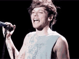 a man in a tank top is singing into a microphone on a stage .