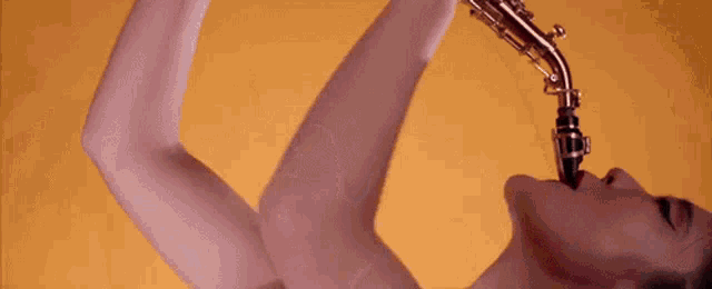 a woman is playing a saxophone with her mouth open against a yellow background .