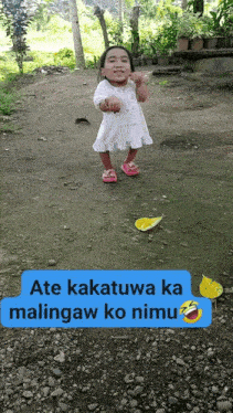 a little girl in a white dress and pink sandals is standing on a gravel road