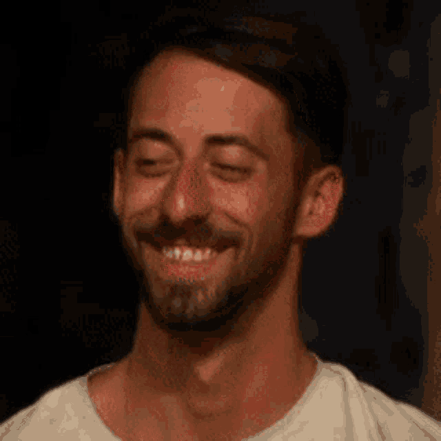 a man with a beard is smiling with his eyes closed and his mouth open .