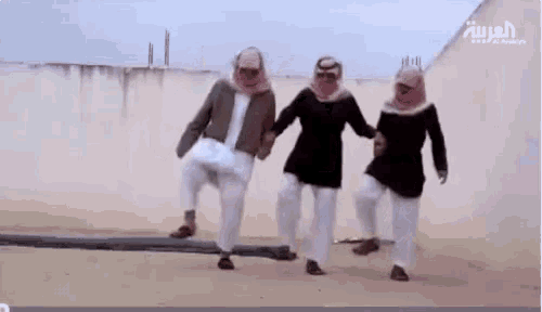 three men in traditional arabic clothing are dancing in the desert .