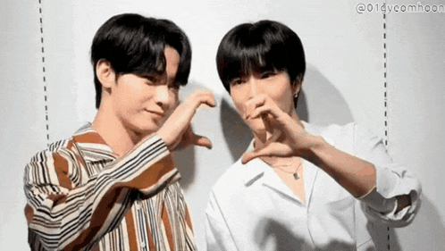 a couple of young men are making a heart shape with their hands .