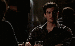 a man is sitting at a table in a dark room with a glass of water in his hand .