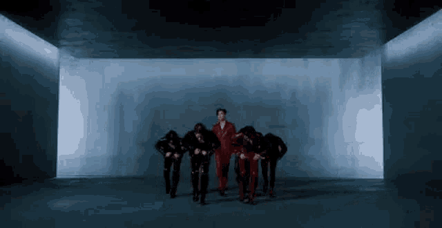 a man in a red suit is standing in a dark room with a group of dancers .