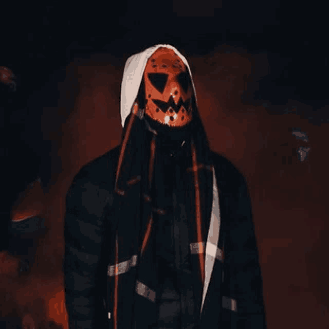 a man is wearing a pumpkin mask and a hood .