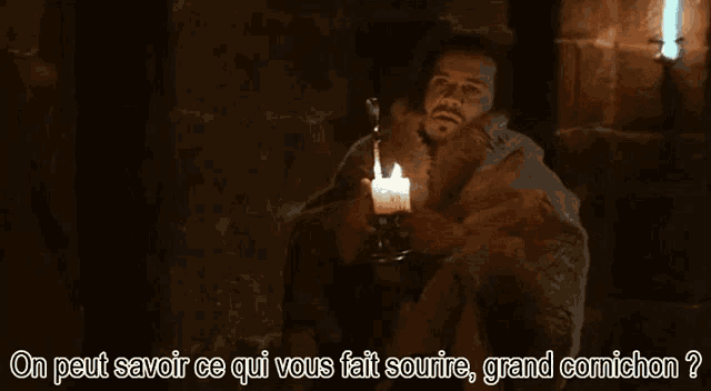 a man is sitting in a dark room holding a lit candle in his hand .