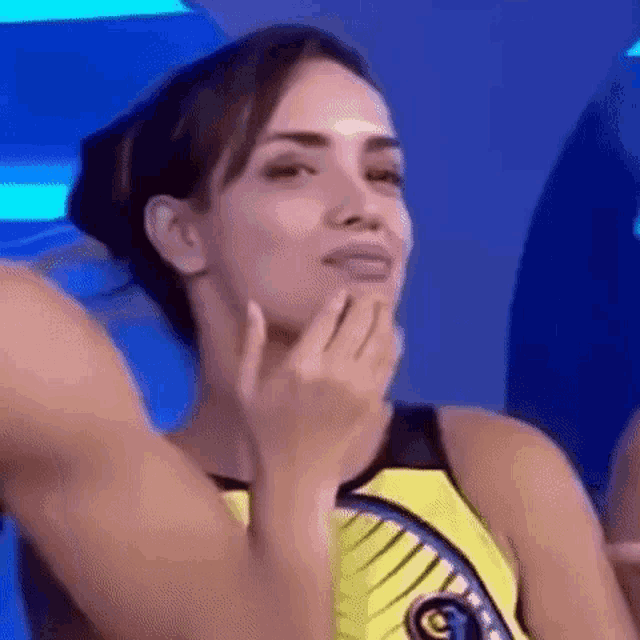 a woman in a yellow tank top is making a funny face with her hand on her face .