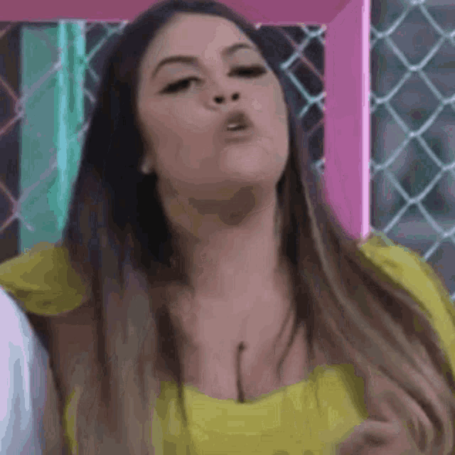 a woman in a yellow top is making a funny face in front of a chain link fence .