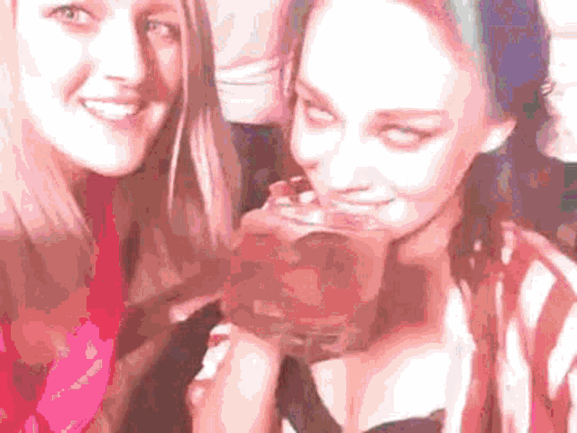 two young women are posing for a picture while one of them is drinking from a glass .