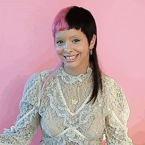 a woman with pink and black hair is smiling and wearing a lace top