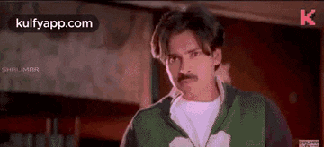 a man with a mustache is wearing a green sweater and a white shirt .
