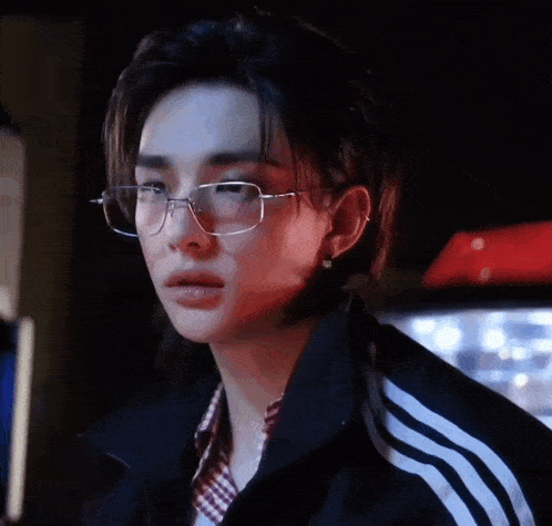 a young man wearing glasses and a black jacket .