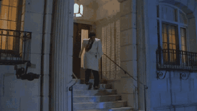 a man in a white coat is running down stairs at night