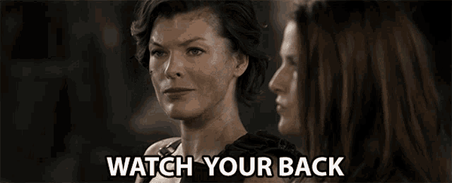 two women are looking at each other and the words watch your back are visible