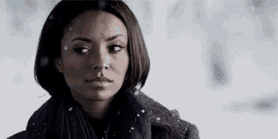 a woman wearing a scarf and a coat is standing in the snow and looking at the camera .