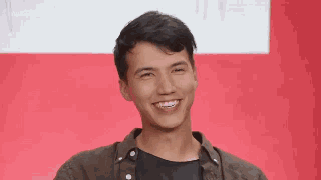 a young man is smiling and looking at the camera while standing in front of a red wall .