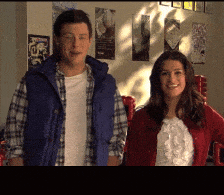 a man wearing a blue vest stands next to a woman wearing a red sweater