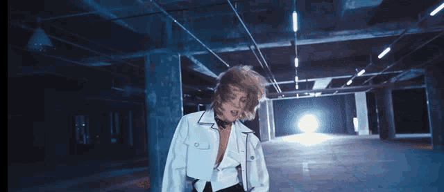 a woman in a white jacket stands in a dark room with her hair blowing in the wind