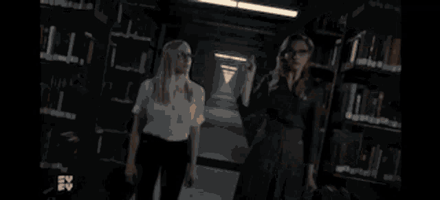 two women are standing next to each other in a dark room in front of a fire .