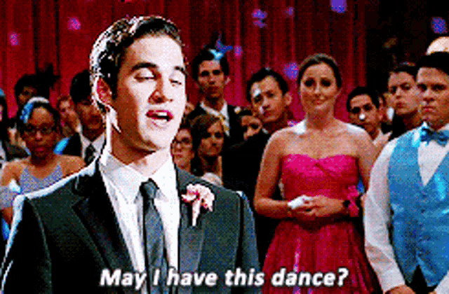 a man in a suit and tie is standing in front of a crowd and saying may i have this dance